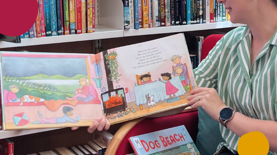 A woman reading a picture book with bookshelves in the background.