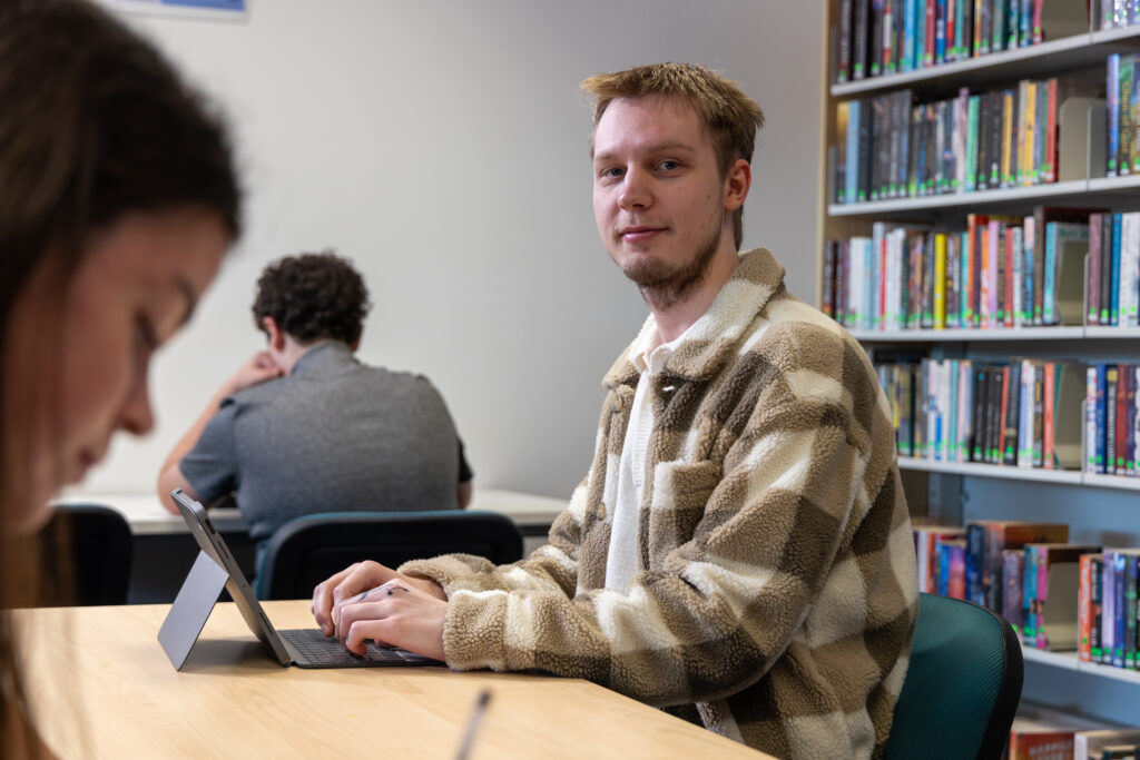 Ypung man looking at camera on his ipad in the library at Bowral
