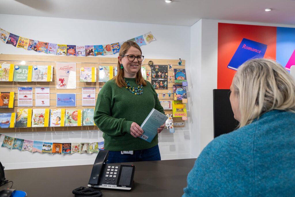 Two women at the library desk smiling and having a conversation.