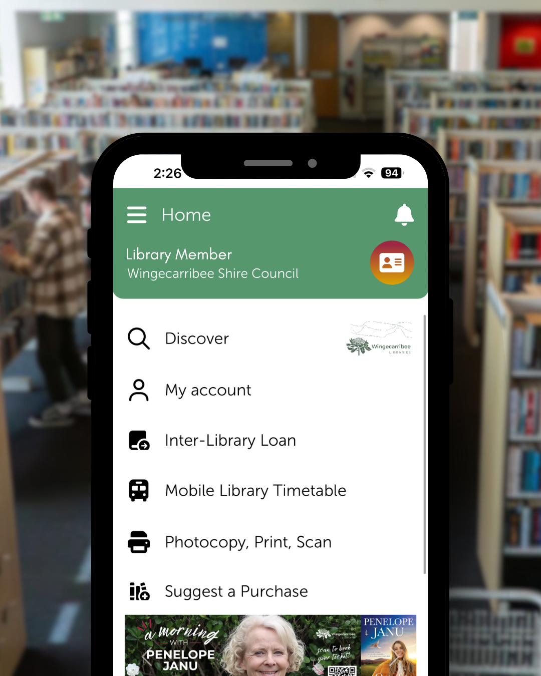 Spydus Library App on a phone screen with library shelves in the background.
