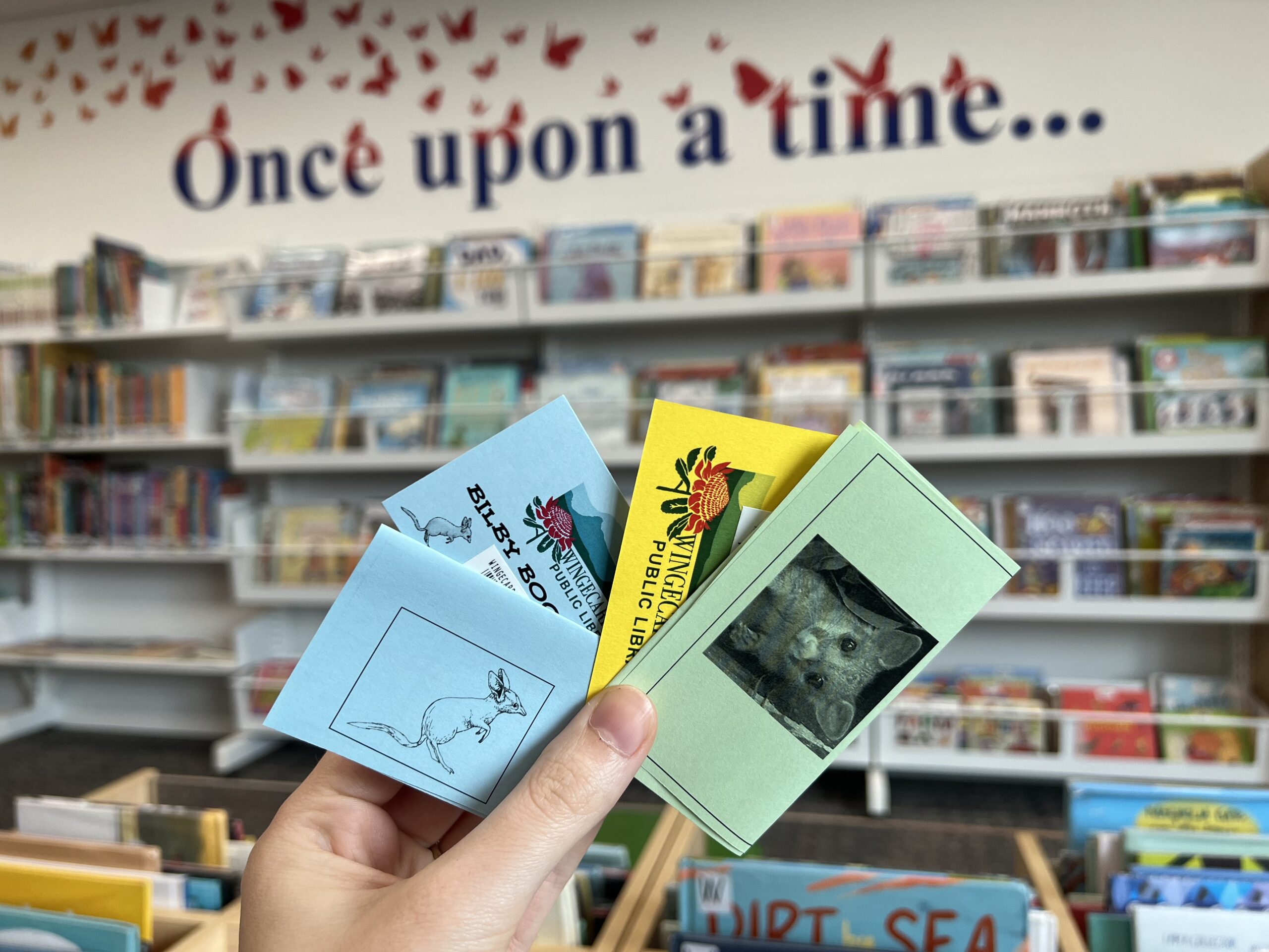 Bilby and Possum passports and library cards with picture book shelving in the background.