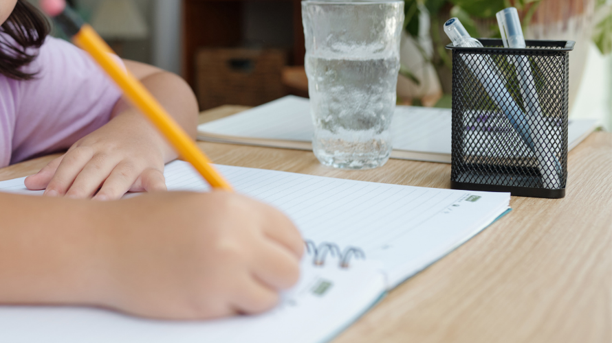 A student sitting at a desk with a pencil and notepad doing homework.