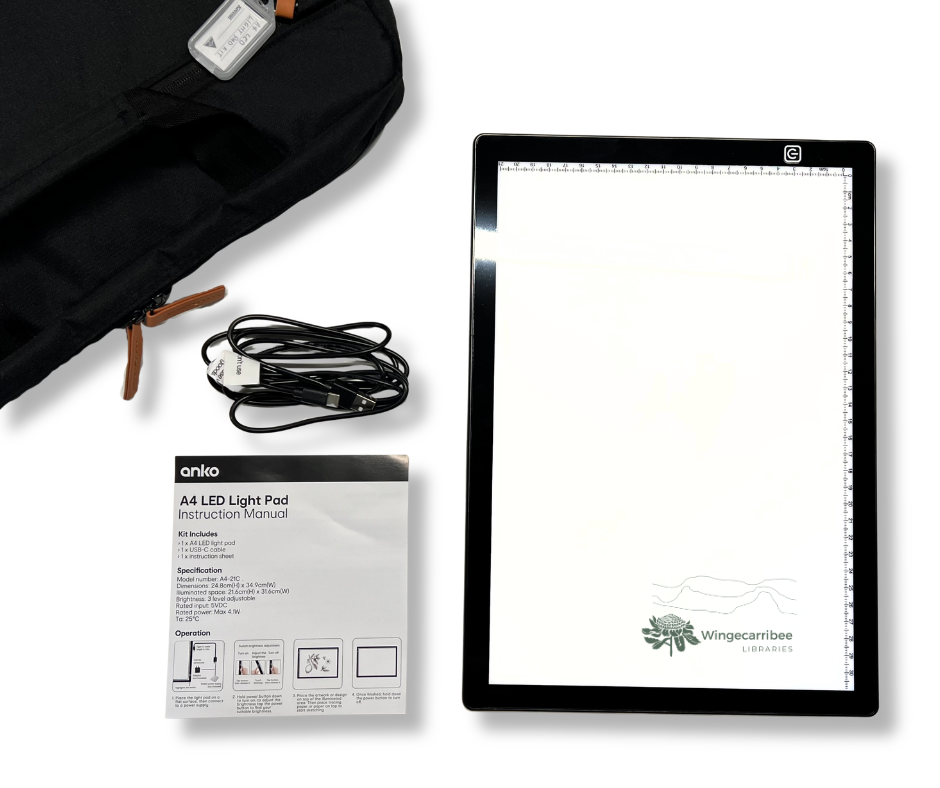 A4 LED Light Pad Kit: a black laptop bag in the top left corner, with the light pad sitting flat on a table with the power cord and an instruction sheet.