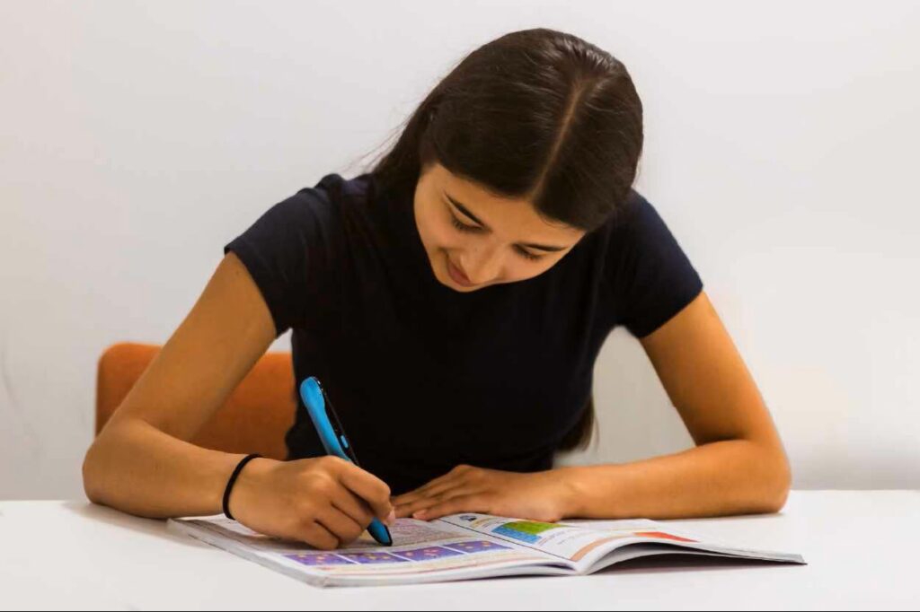 A girl sitting at a table reading a book with a C-Pen reader.